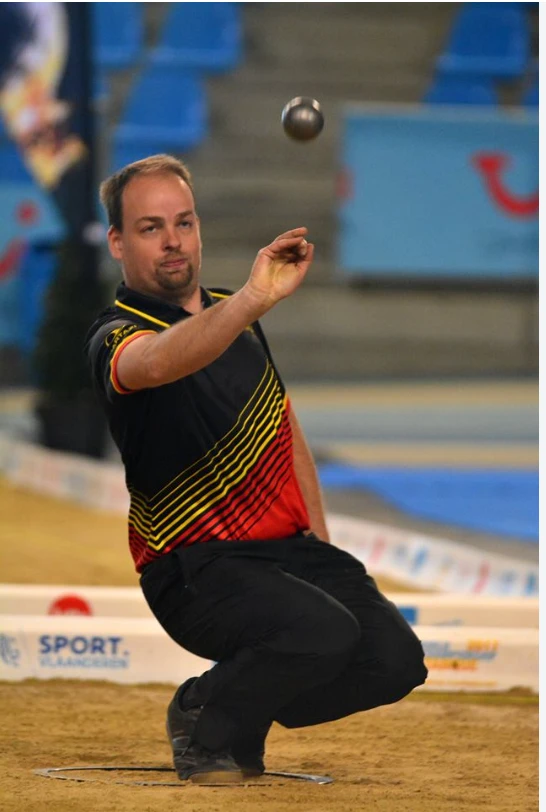 Belgische speler in een diepe hurk net na de worp van zijn boule